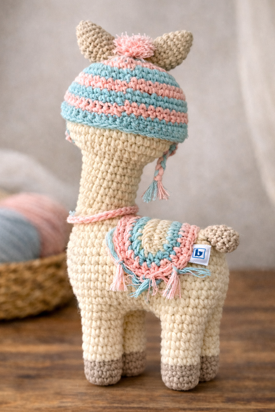 Crocheted llama toy with a colorful hat and scarf on a wooden surface.